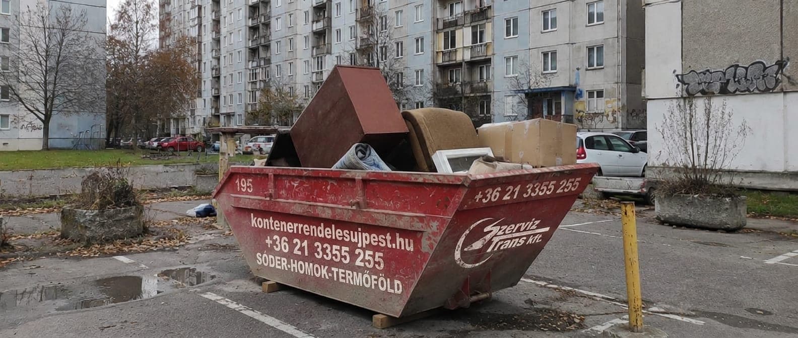 Piros konténer egy újpesti lakótelep parkolójában, lomtalanításból származó bútorokkal — lomtalanítás a IV. kerületben